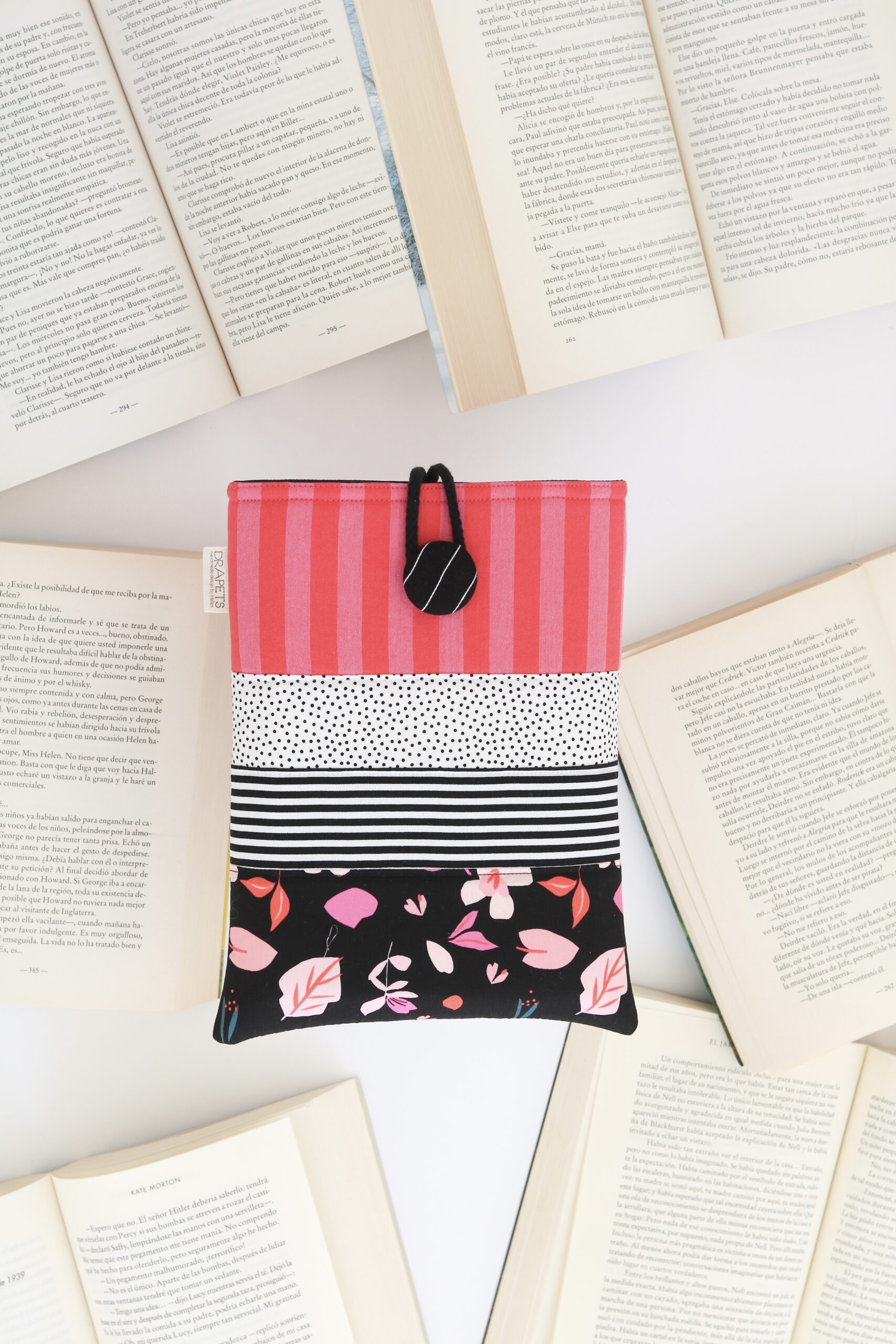 Funda de libro confeccionada con distintas telas en tonos rosa, rojo y blanco y negro. Funda acolchada y única para proteger tus libros. El regalo perfecto para los amantes de la lectura.