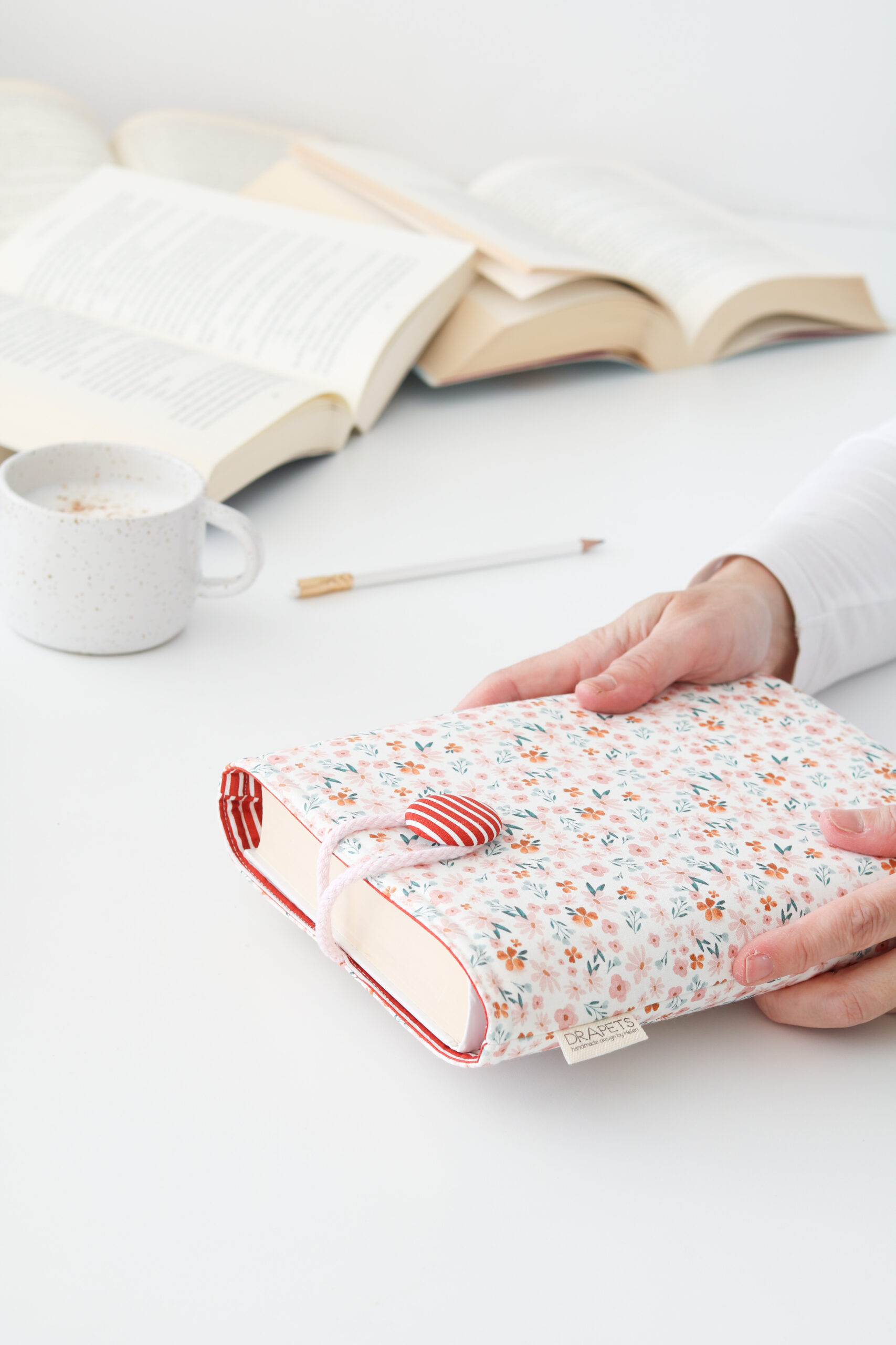 Funda de Libro confeccionada con tela estilo romántico de flores en rosa, toques verdes y teja combinada con un forro interior de rayas en blanco y teja. Funda acolchada para proteger tus lecturas.